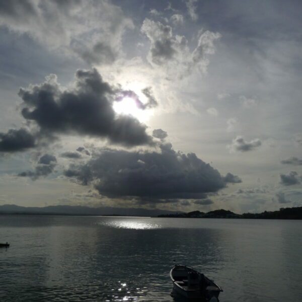 Photographie d'un coucher de soleil sur la mer de Guadeloupe. Les couleurs des nuages et de la mer sont grise et bleu. On peut voir en premier plan un barque.